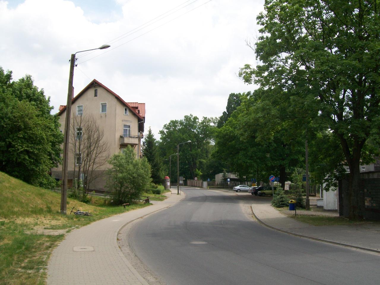 fot. wasiukibic 
Dawny przejazd kolejowy przez ul. Jana III Sobieskiego. Nawierzchnia kolejowa zlikwidowana, podobnie jak szlabany i sygnalizacja ostrzegawcza, ostały się ino zardzewiałe barierki ochronne, widoczne z lewej strony kadru.Tor na teren zakładu wchodził między żółto-niebieskim kubełkiem, a stojącymi za nimi iglakami. Z lewej strony zaś przemykał między barierkami. Widok w kierunku wschodnim - w prawo DZM, w lewo stacja Szprotawa. Obraz