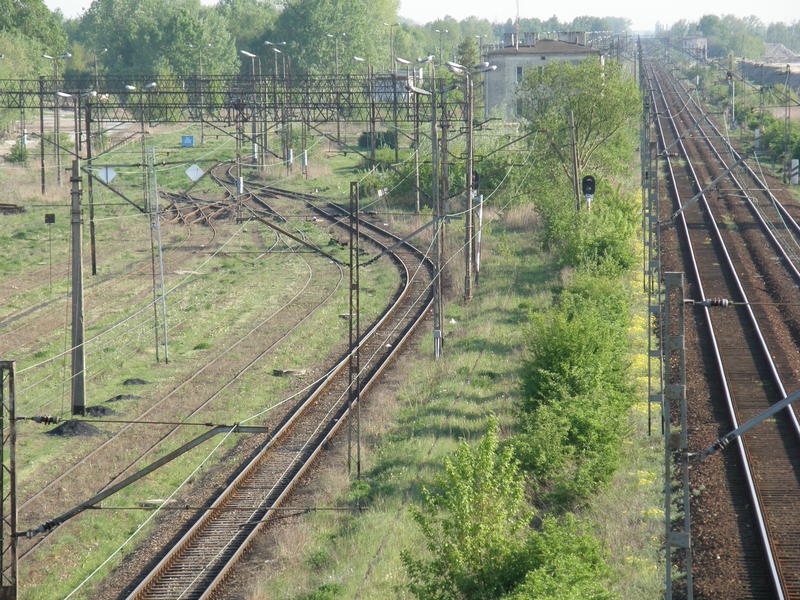fot. Przemysław Więcek 
Głowica 13,7 km. Widok w kierunku Piaseczna. Po prawej tory szlakowe. Po lewej tory stacyjne dla ruchu towarowego obsługiwane przez nastawnie OK2 w km 12,8 i OK4 w km 13,9. Widoczne tory pomiędzy dwiema grupami torów towarowych. Na wprost budynek PKP Cargo S.A. Zakład Przewozów Towarowych w Warszawie. Sekcja Przewozów i Ekspedycji Warszawa Główna Towarowa. Kasa towarowa. Posterunek odprawy pociągów. Posterunek rewizji technicznej wagonów. Stacja Warszawa Okęcie. Obraz