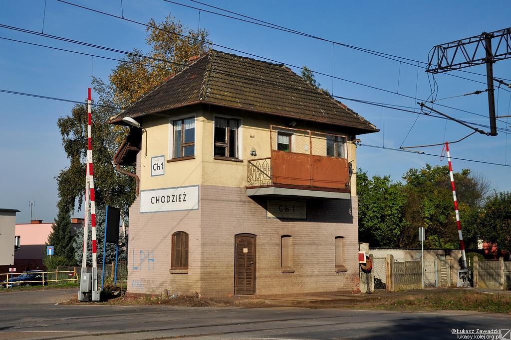 fot. Lukasy 
Nastawnia wykonawcza w Chodzieży stojąca przy wjeździe od strony Rogoźna Wielkopolskiego/Poznania i przy przejeździe kolejowym z ul. Ujską. Widoczna z prawej strony kadru mechaniczna rogatka, która strzegła przejścia dla pieszych, przeszła do historii w kolejnym roku. Obraz