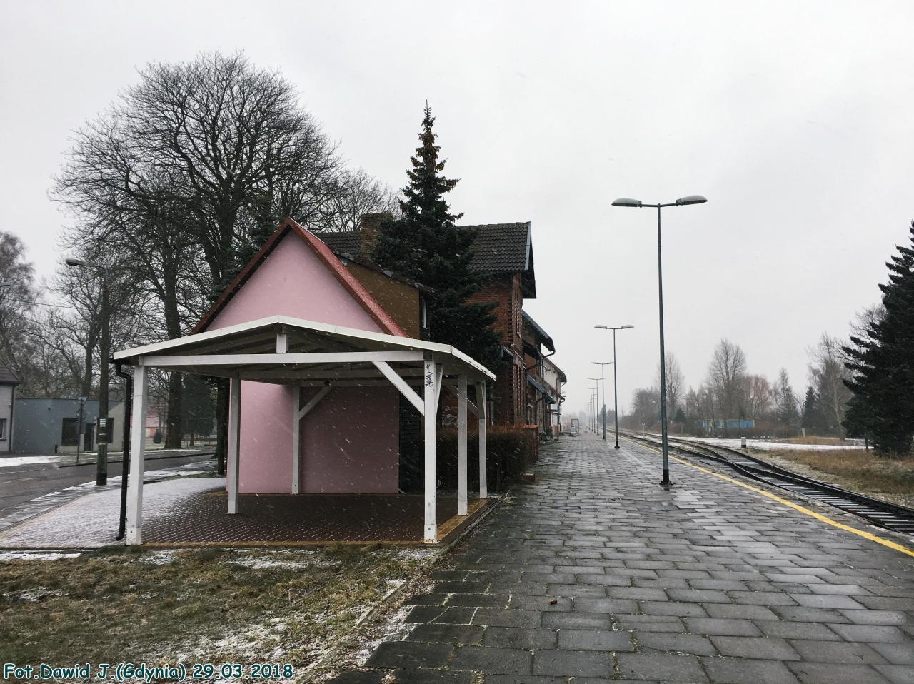 fot. Dawid Jastrzębski 
Widok z peronu w kierunku Lęborka. Kolejowy budynek mieszkalny (Plac Dworcowy 1), kolejowy budynek mieszkalny (Plac Dworcowy 3) z przyległą częścią z pomieszczeniami WC i budynek dworcowy, znajdują się po lewej stronie. Obraz