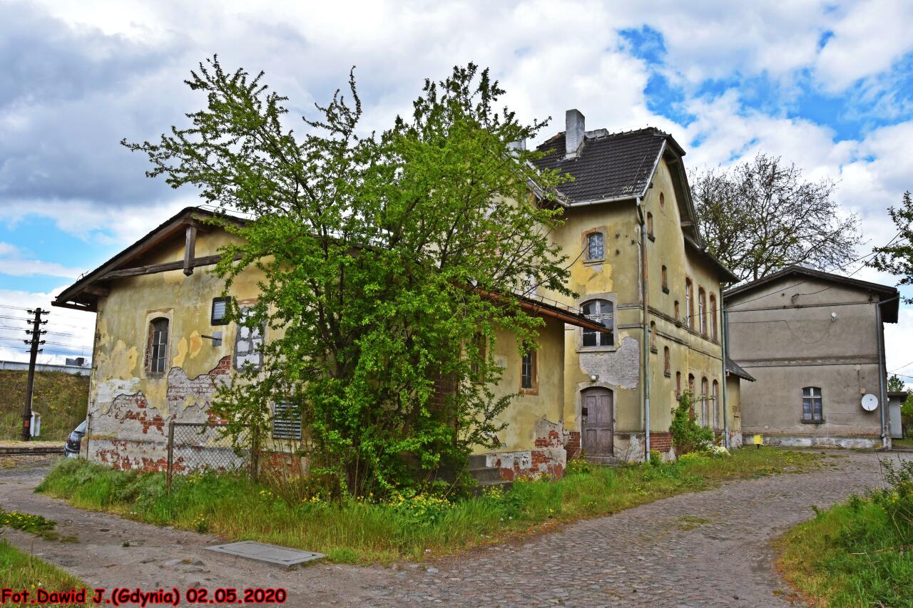 fot. Dawid Jastrzębski 
Budynek dworcowy z przyległym budynkiem magazynu i kolejowy budynek mieszkalny (Ostaszewo 1c). Obiekty widoczne od strony podjazdu. Widok w kierunku Chełmży/Malborka. Obraz