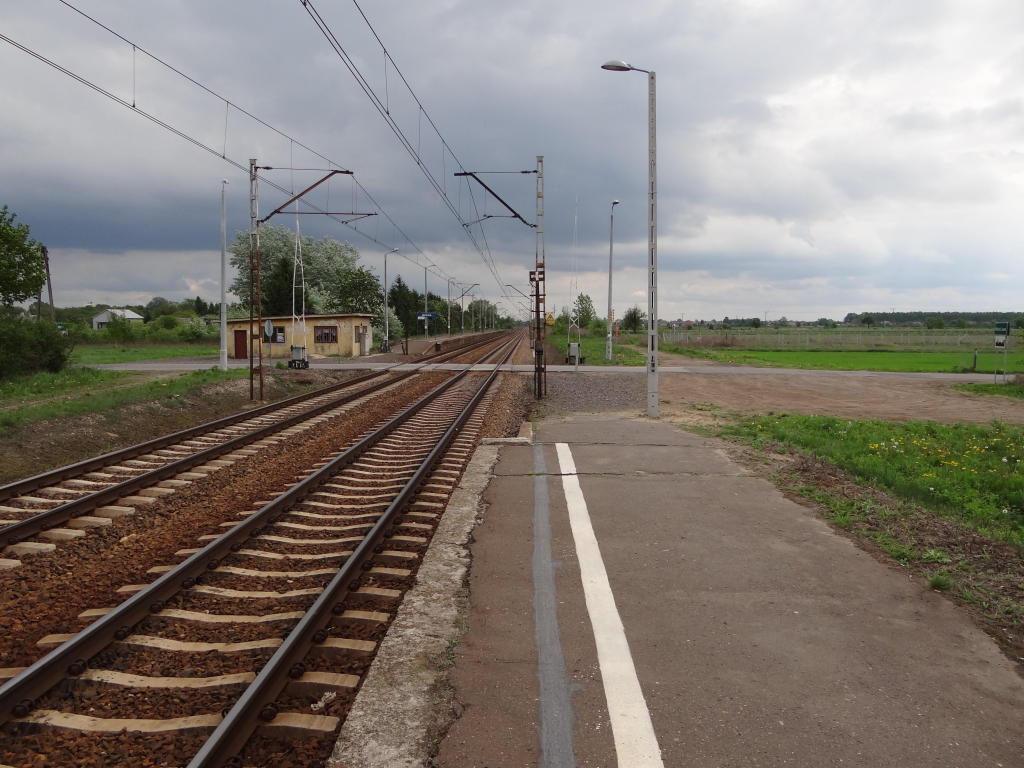 fot. Przemysław Więcek 
Peron dla pociągów w kierunku Skierniewic (bliżej). Parking na ok. 10 miejsc. Przejazd drogowy w Mokrej. Budynek dworcowy. Peron dla pociągów w kierunku Łowicza. Widok w kierunku Skierniewic. 4,1 km. Obraz